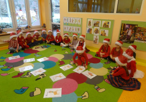 Grupa dzieci siedzi wokół ilustracji rozłożonych na dywanie, dziewczynka przekłada ilustrację.